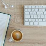 Tasse de café, un notebook, des écouteurs et un clavier sur un bureau en bois clair