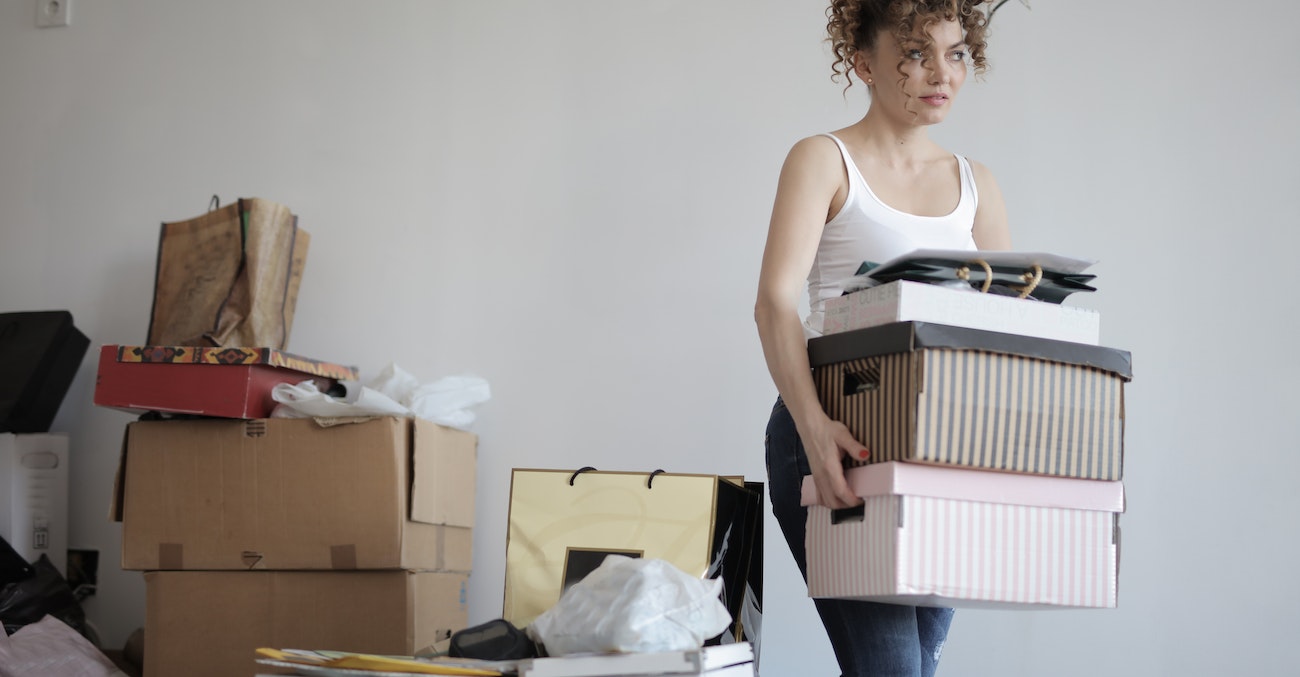 Femme qui tient des cartons, avec également des cartons à l'arrière plan.